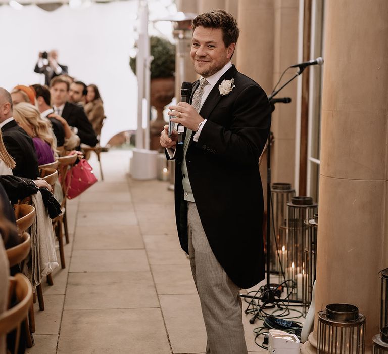 Grooms stands with microphone as he reads out his speech in morning suit 