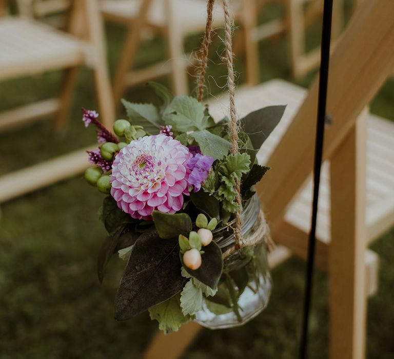 Small glass mason jars full of pink and purple flowers hanging on string for aisle wedding decoration 