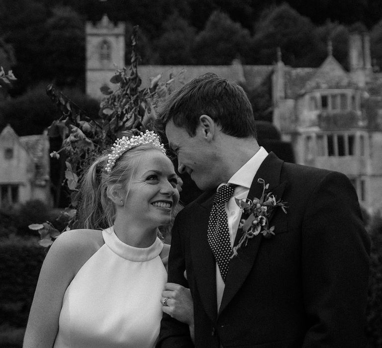 Bride and groom link arms and smile at each other with groom in morning suit and bride in halter neck wedding dress 