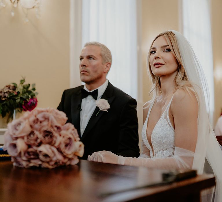 Bride and groom seated during their wedding ceremony as they prepare to sign the register 