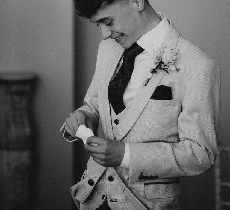 Ring bearer gets the rings out of a white pouch in a grey suit jacket and blue tie and handkerchief 