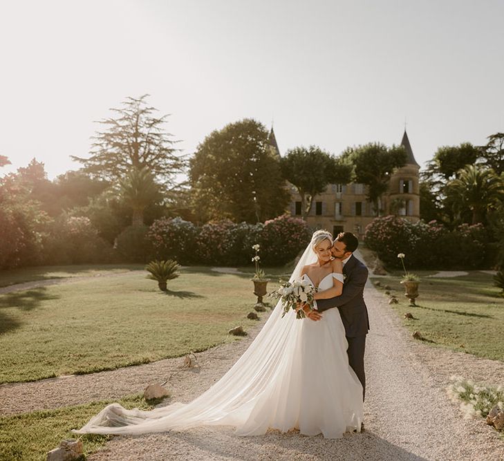 Bride & groom embrace in front of Chateau de Robernier for couples portraits in the sunshine 