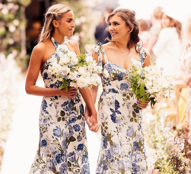 Bridesmaids in white and blue floral dresses holding hands walking down the aisle for the wedding 