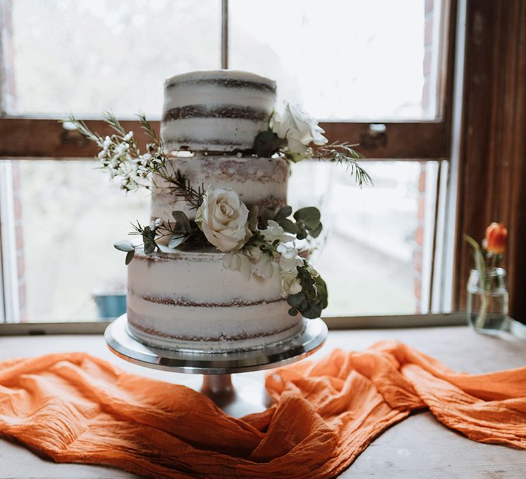 Three-tier naked wedding cake with floral decor on burnt orange table runner