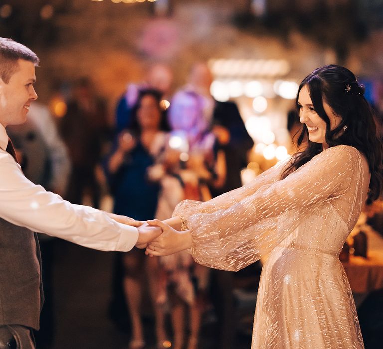 Bride & groom dance beneath festoon lighting during barn wedding reception