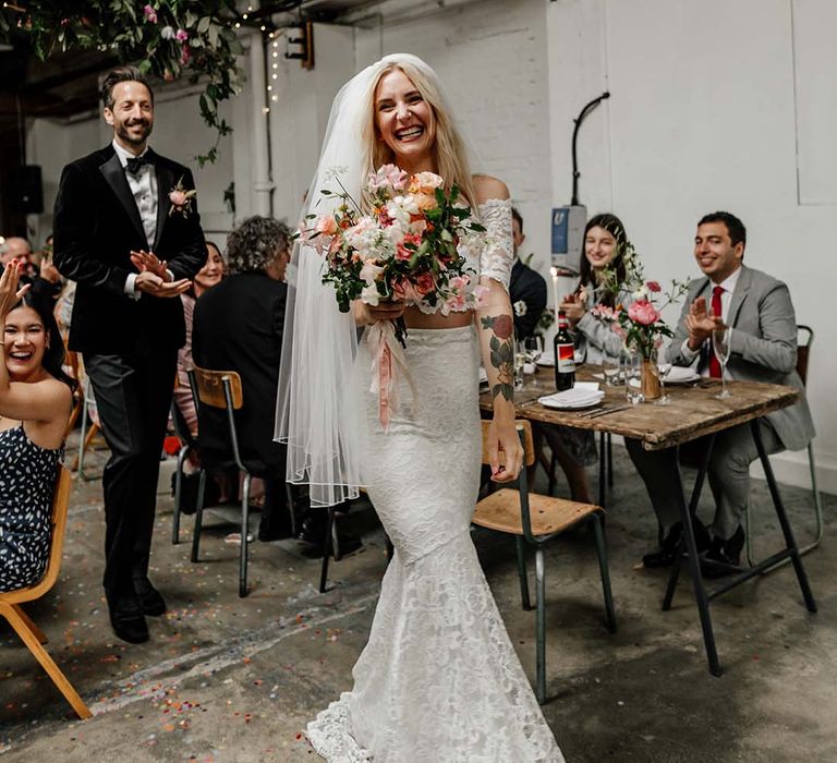 Bride in boho two piece lace bridal outfit with large colourful mixed bouquet laughing and smiling during wedding reception