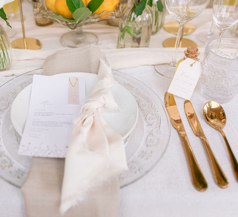 Patterned clear charger plates with white plate and blush napkin and the wedding menu with gold cutlery and yellow wedding flowers 