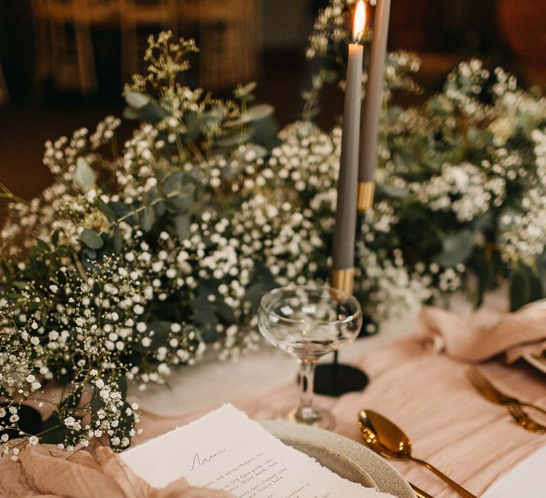 Wedding menu with neutral pink napkin, rose gold cutlery and sage green ceramic plates in front of foliage table decorations