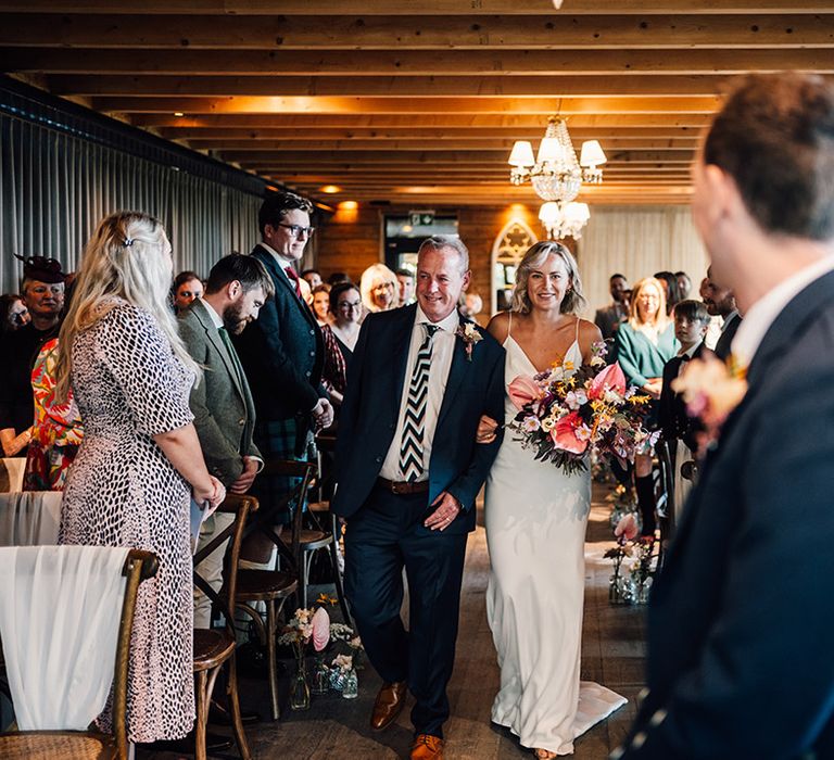 Bride holds tropical bouquet as she walks down the aisle with her father