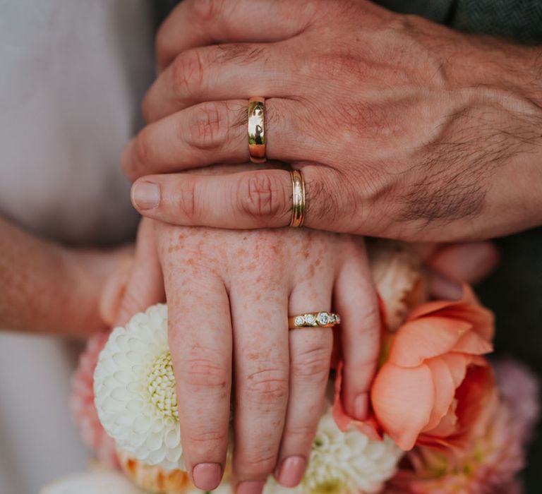 Groom wearing a gold wedding band holding hands with the bride wearing a gold wedding band embedded with diamonds