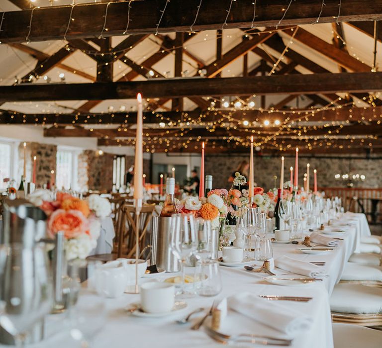 Rustic wedding inspiration with fairy lights the tables are decorated with peach and coral taper candles 