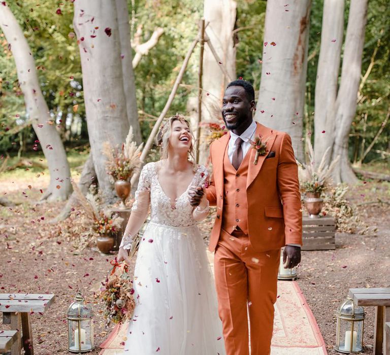 Bride and groom at a harvest wedding doing sustainable confetti walk with pillar candles in large silver candle holders, triangular wooden wedding arch and bronze flower pots