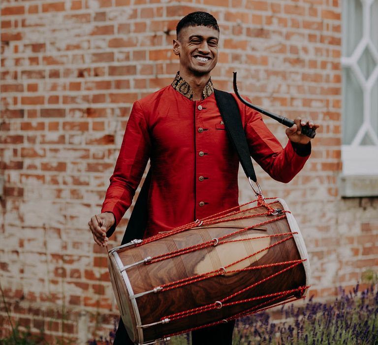 Dhol player in bright red and gold suit plays outdoors 