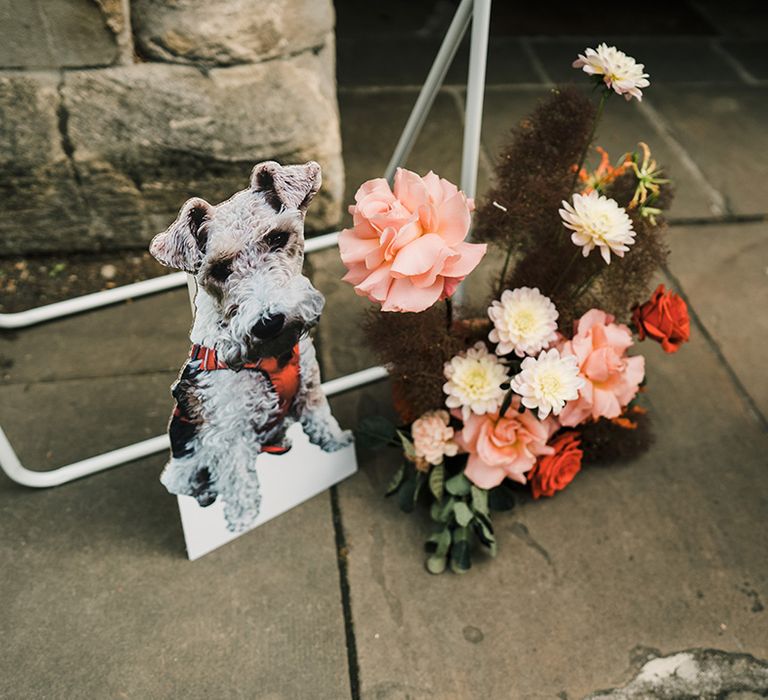 Cardboard cutout of bride & grooms dog beside colourful floral arrangements 