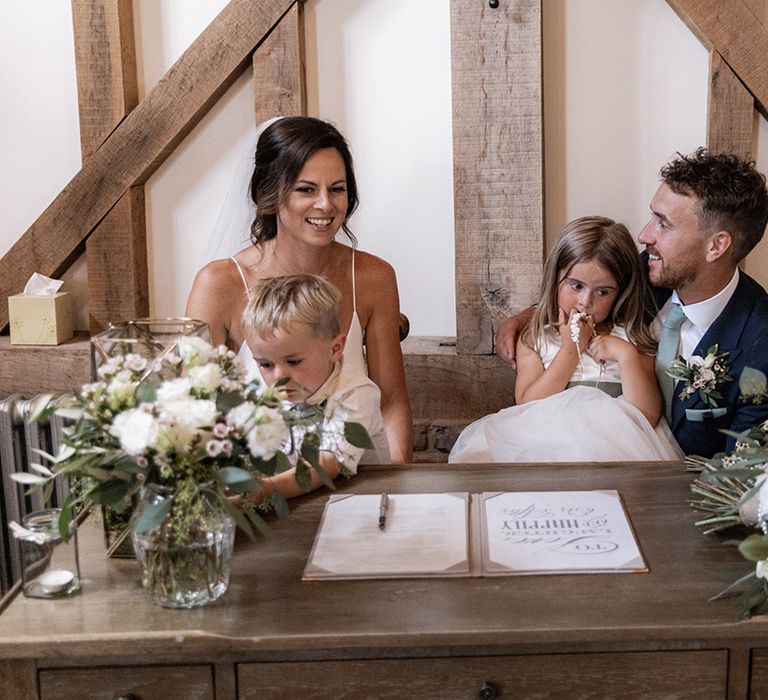 Chloe Bruce & her husband sit with their children as they sign marriage certificate after barn wedding ceremony