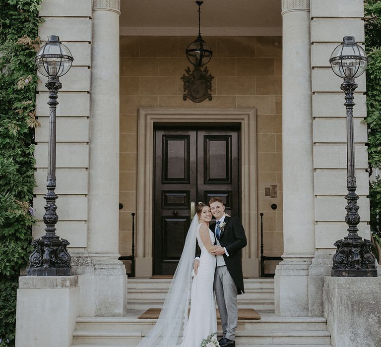 Bride & groom stand in front of grand entranceway to Hedsor House for classic wedding 