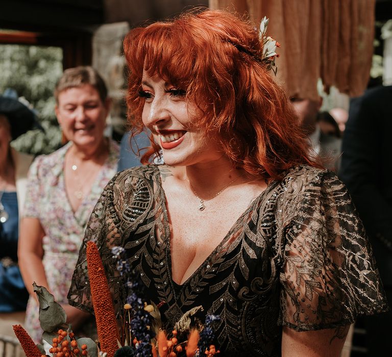 Bride in embellished v-neck black dress for wedding in Devon with orange and yellow dried flower wedding bouquet 