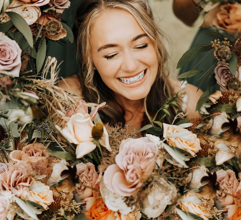 Autumnal wedding flowers with the bride smiling in brightly in the middle of the flower arrangement 