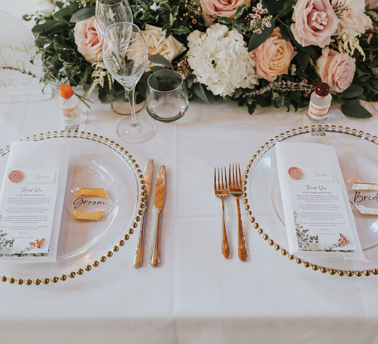 Table place settings with gold beaded charger plates, gold cutlery, DIY place names with pink and gold touches, with charity wedding favours 