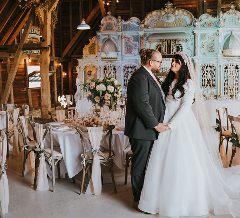 The bride in a high neck long sleeve wedding dress stands with the groom in a dark grey suit and pink tie at their wedding reception with a pastel pink and green wedding theme 