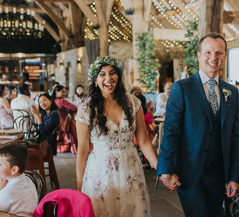 British Indian bride in a Savin London Amelia Dress entering the wedding reception with her groom in a light blue suit 