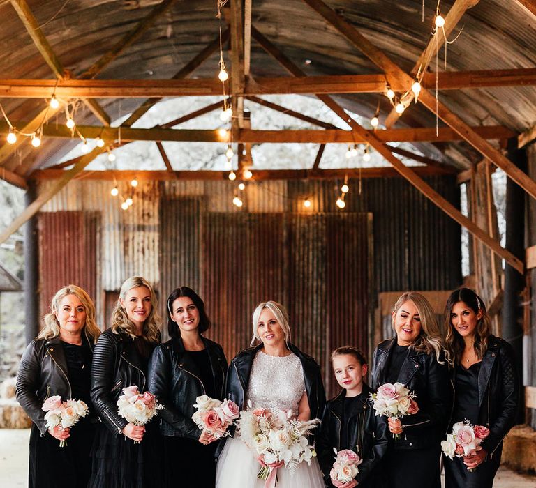 Bridesmaids with side swept hair in black bridesmaid dresses and black leather jackets with the bride in bridal separates with pale pink rose bouquets