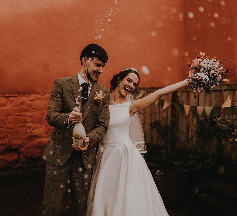 The groom pops champagne to celebrate the wedding day in Devon with a rustic romance wedding theme 