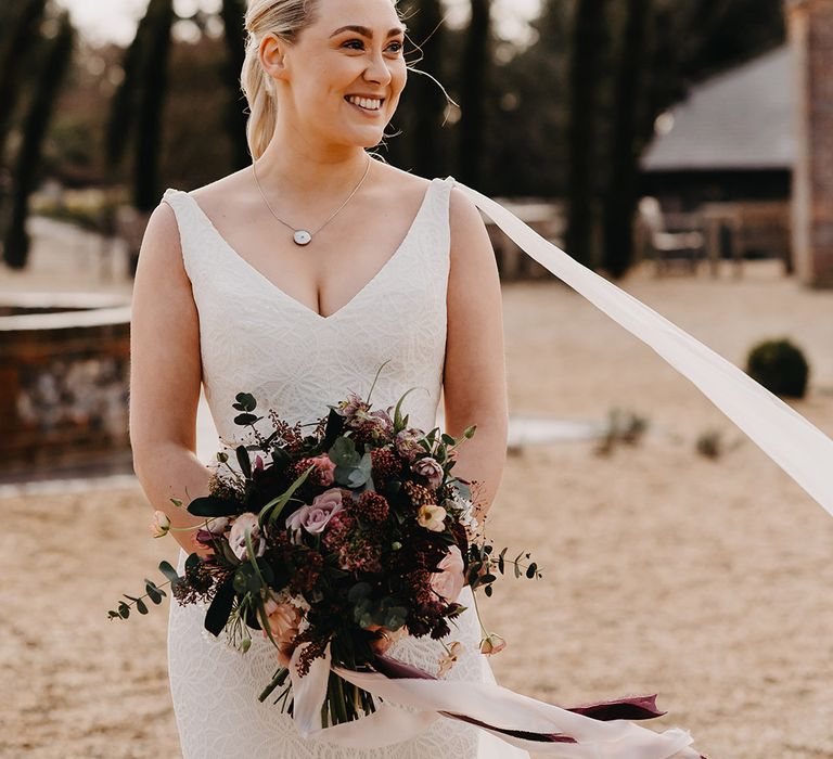 Bride in floral lace wedding dress holding a purple and pink round wedding bouquet tied with ribbon 