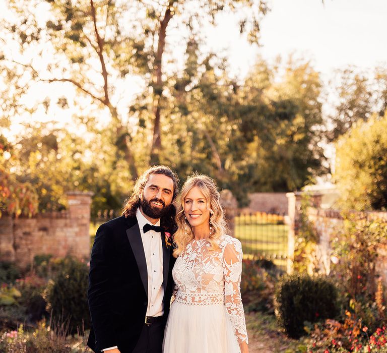 Bride in long sleeve lace wedding dress embracing groom in black tie suit for their couple portraits 