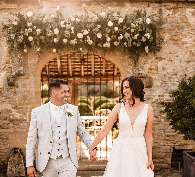 rustic luxe wedding at Caswell house with bride in a princess wedding dress and groom in a light grey check suit holding hands