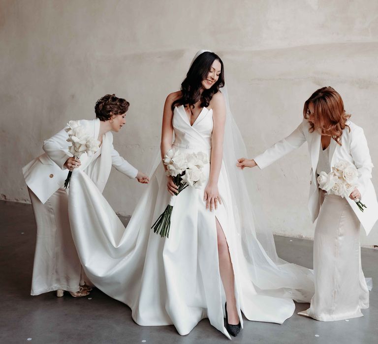 Bridesmaids in white bridesmaid suits fix bride's Suzanne Neville wedding dress at Upton Barn wedding venue