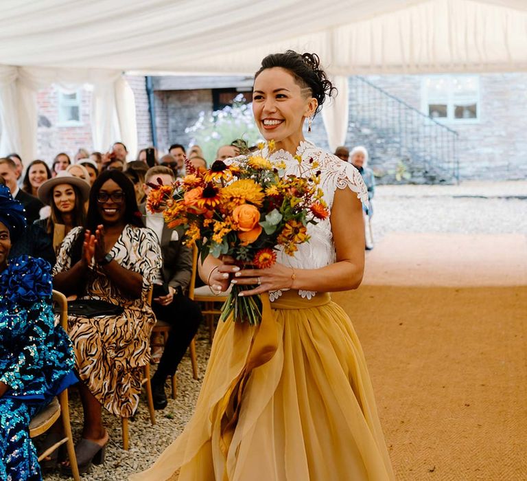 Bride in white mesh lace bridal crop top and yellow wedding skirt holding dried autumnal wedding bouquet with sunflowers, garden roses, pampas grass, eucalyptus, yellow tall kangaroo paws, orange osmanthus flowers, foliage and dried flowers 