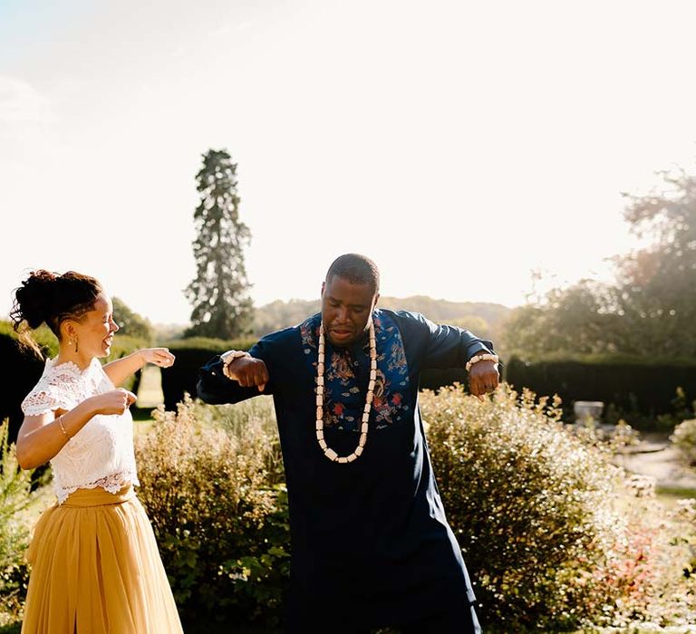 Groom in traditional Nigerian wedding outfit with off-white wedding beads necklace dancing with bride in white mesh lace bridal crop top and yellow wedding skirt at Broadfield Court