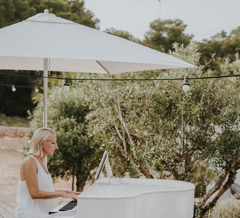 pianist playing at a white piano under a parasol with white wedding flower arrangement decor