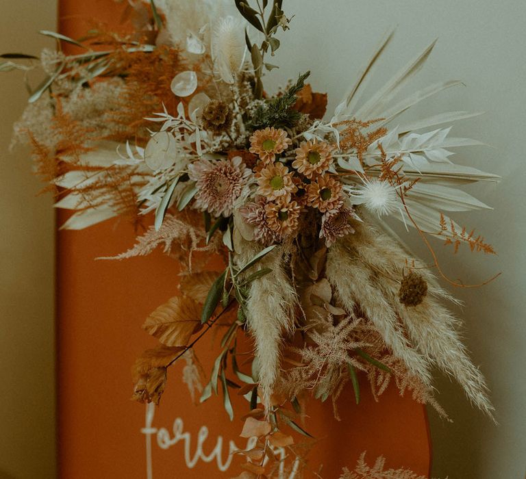 Pampas grass wedding flower arrangement decoration attached to the orange arched wedding seating chart 