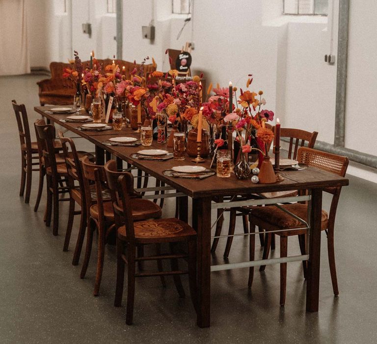 German auction house wedding venue with rustic wedding tablescape with vinyl record place mats, gold rimmed plates, gold cutlery, colourful pink, red and orange floral centrepieces in bottles and tapered candles 