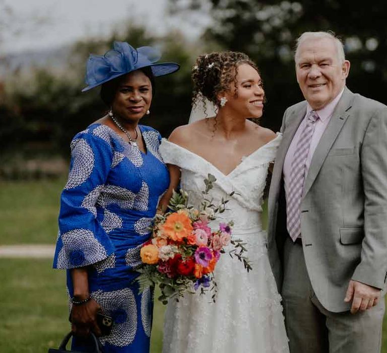 Bride in Suzanne Neville off shoulder 3D floral applique wedding dress standing with her parents at Elmore Court Gloucestershire wedding