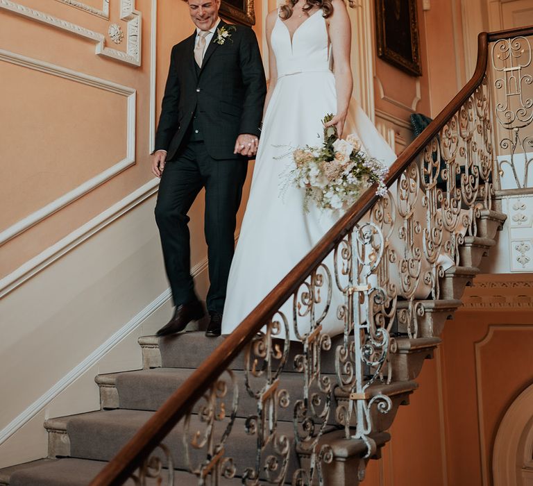 The bride and groom walk down steps at Kelmarsh Hall to enter their reception 