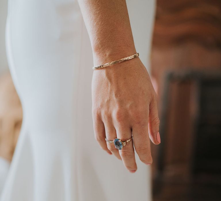 Bride wearing gold bangle bracelet with gold and blue oval diamond ring 