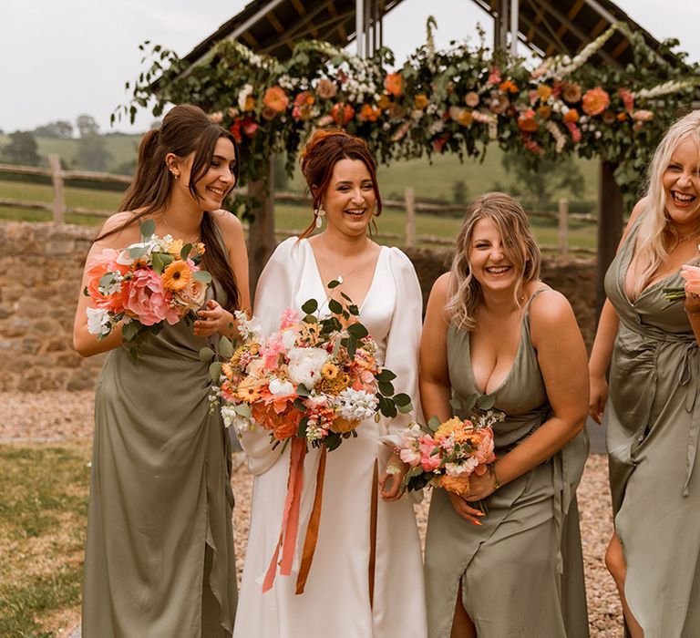 Bridal party in green wrap bridesmaid dresses with bride in balloon sleeve wedding dress holding orange flower wedding bouquets 