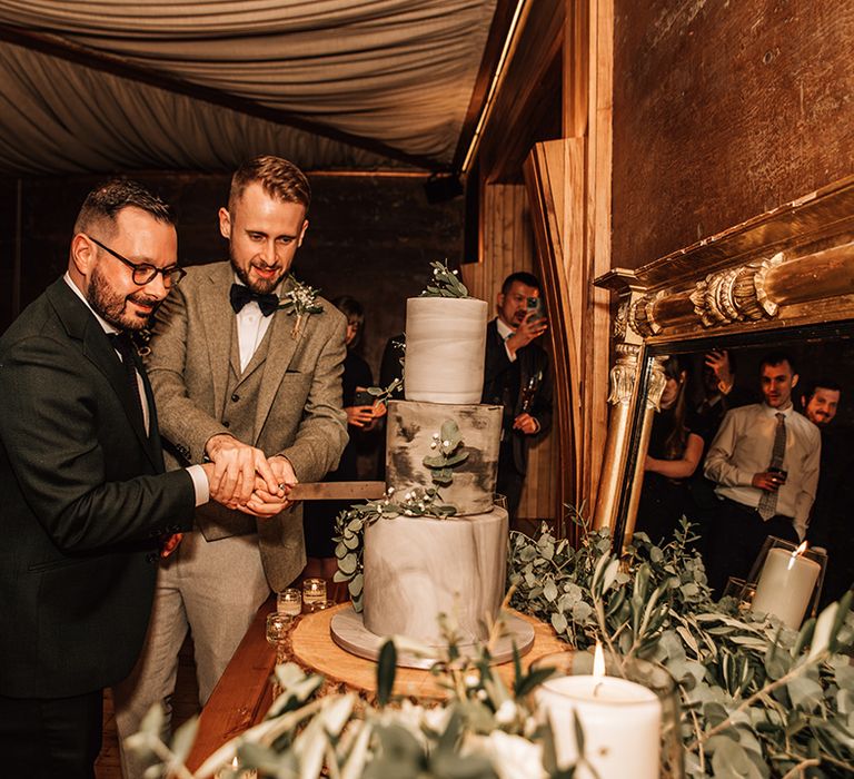 Three tier grey marble wedding cake being cut by the two grooms 