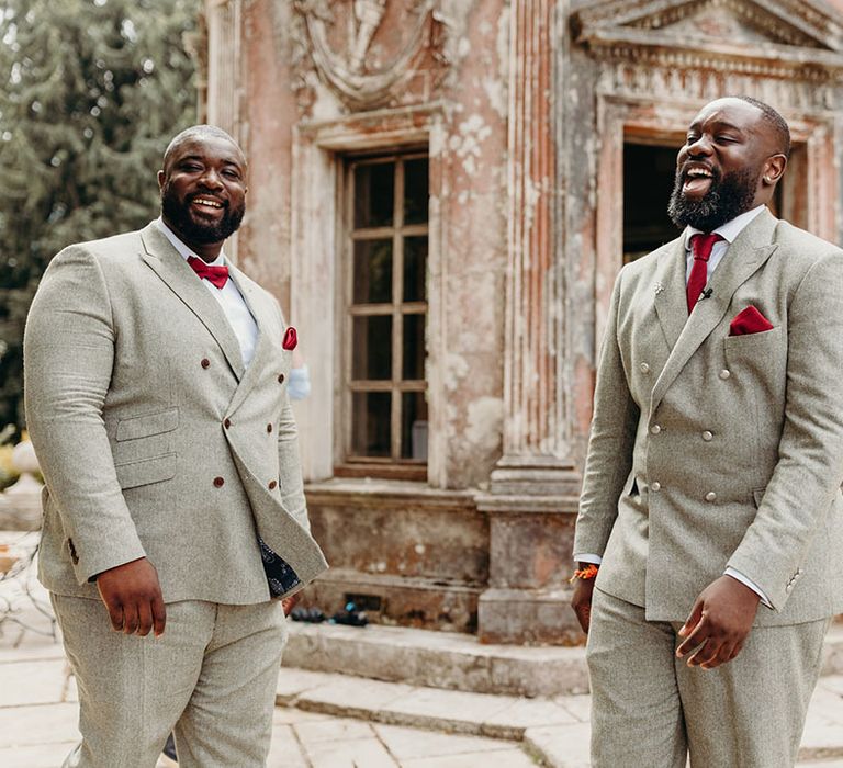 The groom laughs with the best man in matching light grey wedding suits 