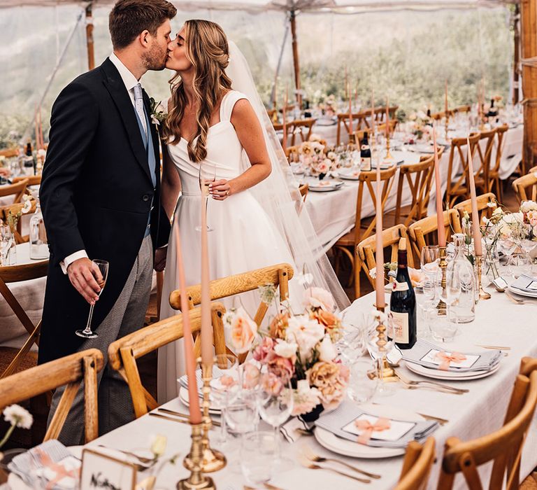 bride and groom kissing in their marquee Sennen Cover wedding reception with wicker lampshade and flower handing installation 