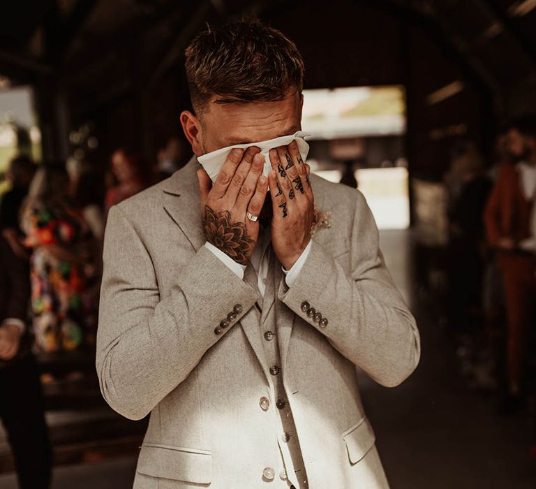 Groom in stone three piece wedding suit crying at the wedding ceremony as he sees the bride 