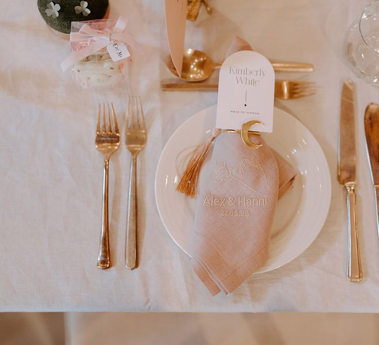 Romantic wedding table setting with lilac wedding napkins, gold cutlery, white plates and arched place name cards 