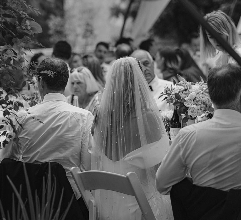 Bride wearing pearl wedding veil sitting at wedding breakfast for outdoor wedding 