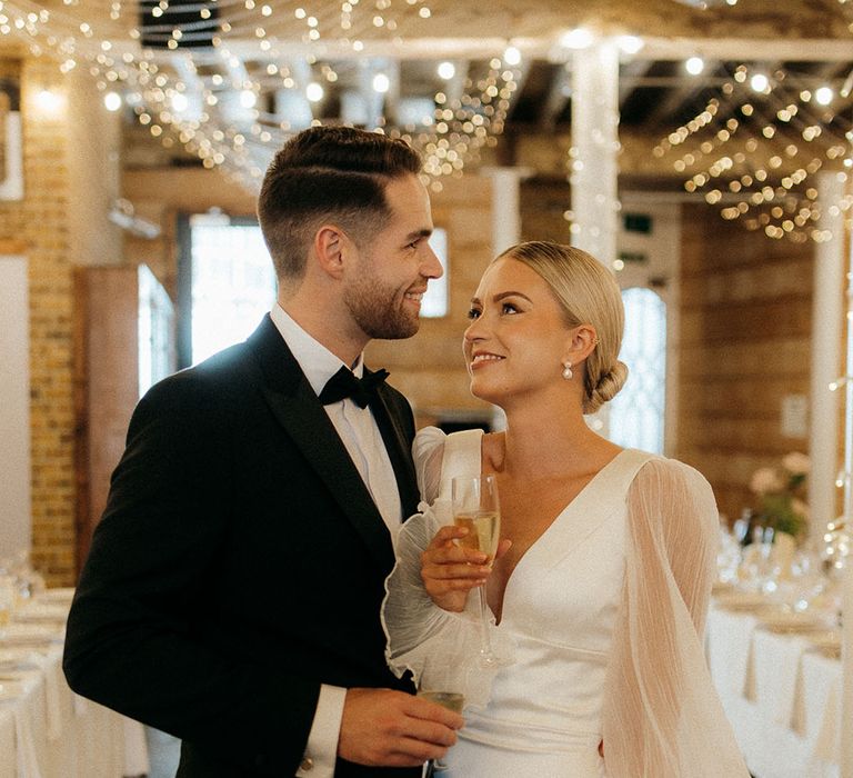 Vintage glam wedding fashion with the bride in sheer long sleeve wedding dress with groom in black tuxedo 