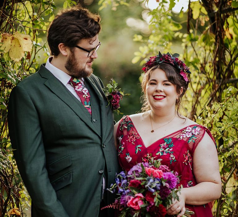 Groom in dark green wedding suit with bride in red wedding dress with flower crown hair accessory 