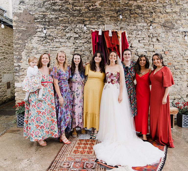 The bride in a floral strapless wedding dress with the wedding guests in colourful guest outfits 