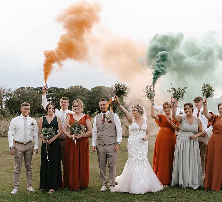 Colourful smoke bomb for barn wedding with the wedding party in orange and green wedding outfits 